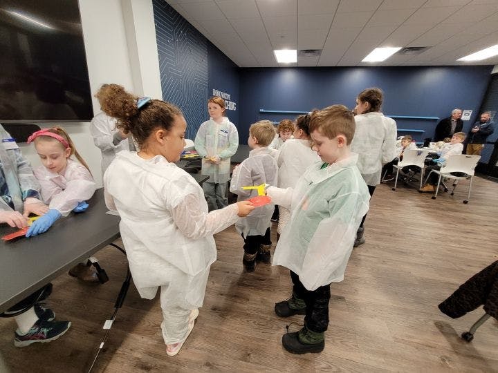 Students in lab coats hold up colored objects, looking for a matching set.