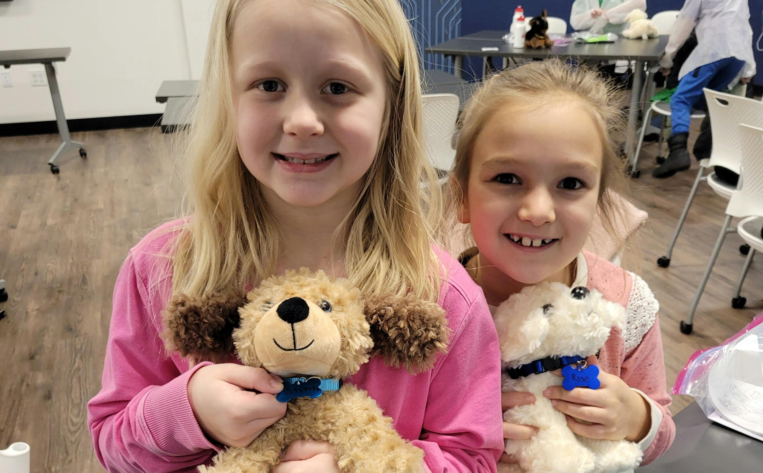 Two school-age children hold stuffed animals while smiling