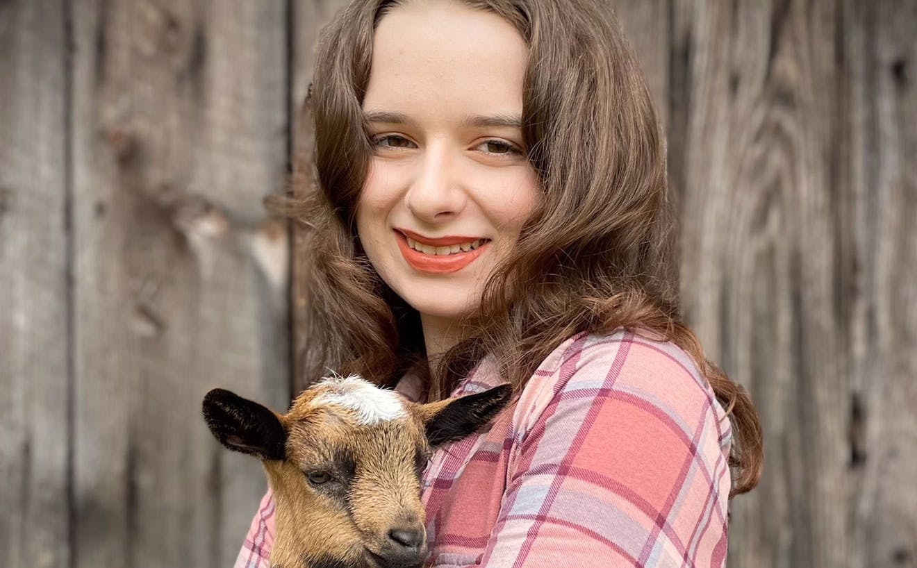 Young woman holding a baby goat, which is wearing a bowtie.